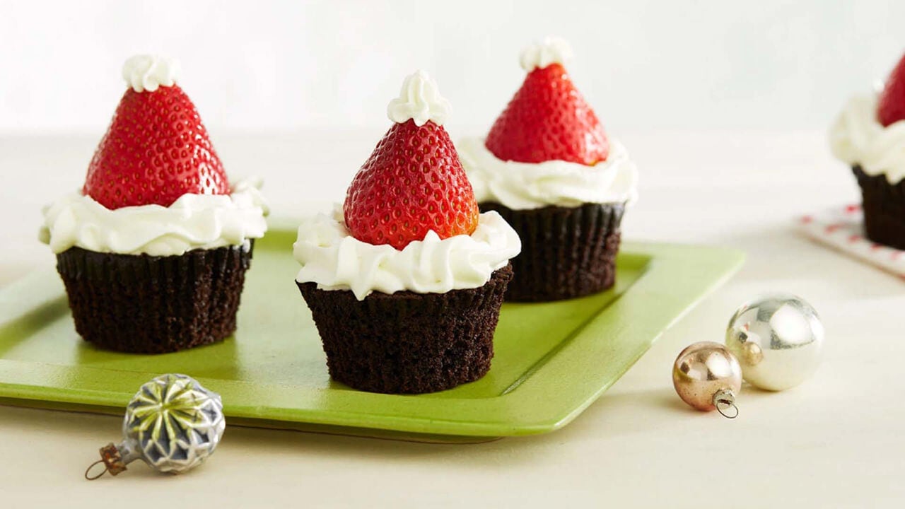 batch of santa hat cupcakes topped with fresh strawberries and vanilla frosting