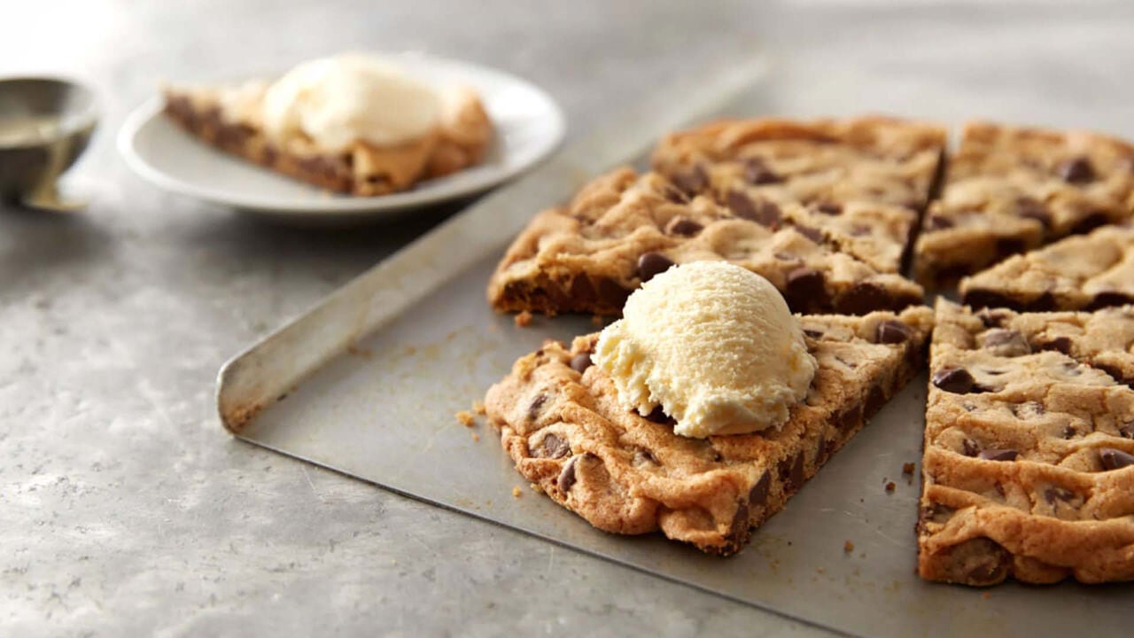 slicing hersheys milk chocolate chip giant cookie into pieces topped with ice cream
