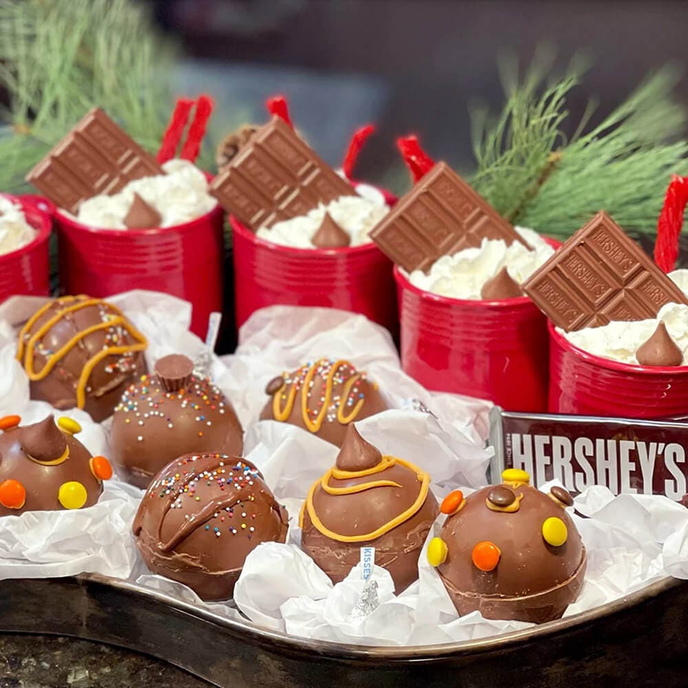 hot chocolate bombs in front of mugs of hot chocolate