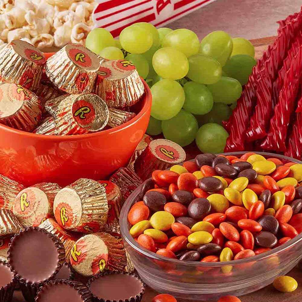 board topped with assorted hersheys candies, salty snacks, and fruit