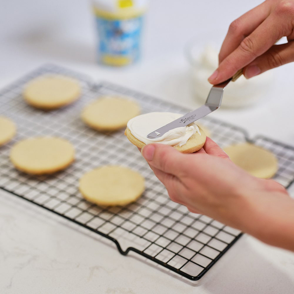 person spreading icing onto the sugar cookies