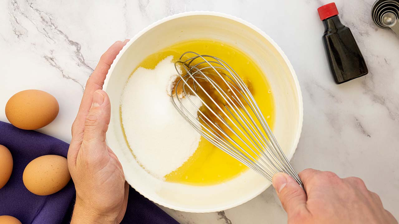 person whisking sugar, vanilla, and butter together in mixing bowl