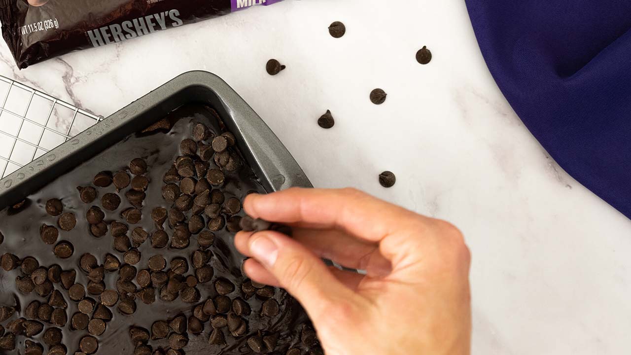 person adding hersheys baking chips on top of the creamy brownie frosting