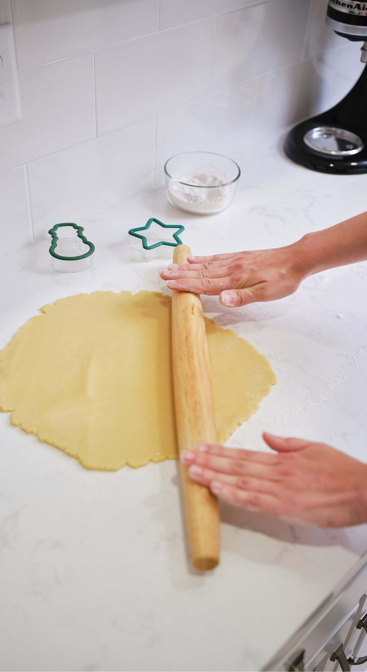 person rolling cookie dough out on the kitchen counter
