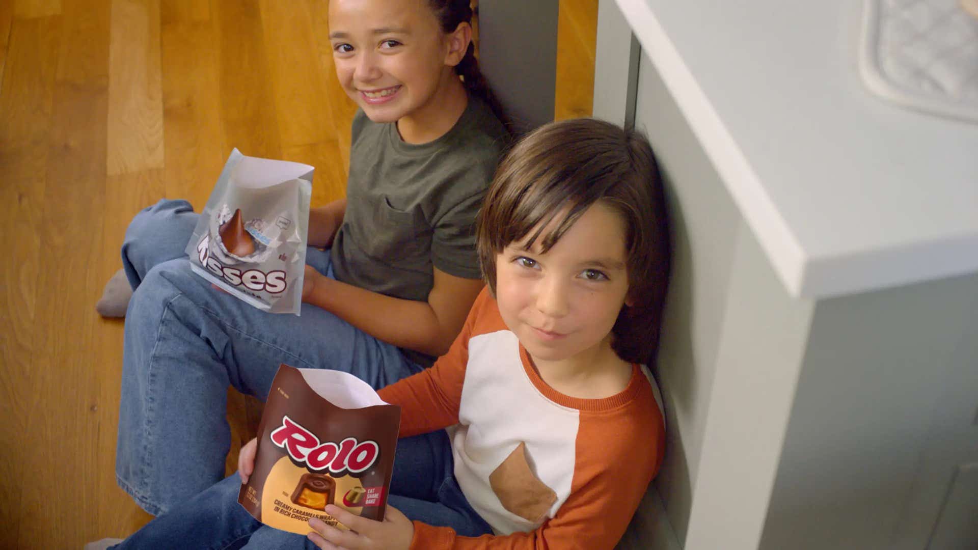 kids sitting on kitchen floor holding bags of hersheys kisses and rolo creamy caramels